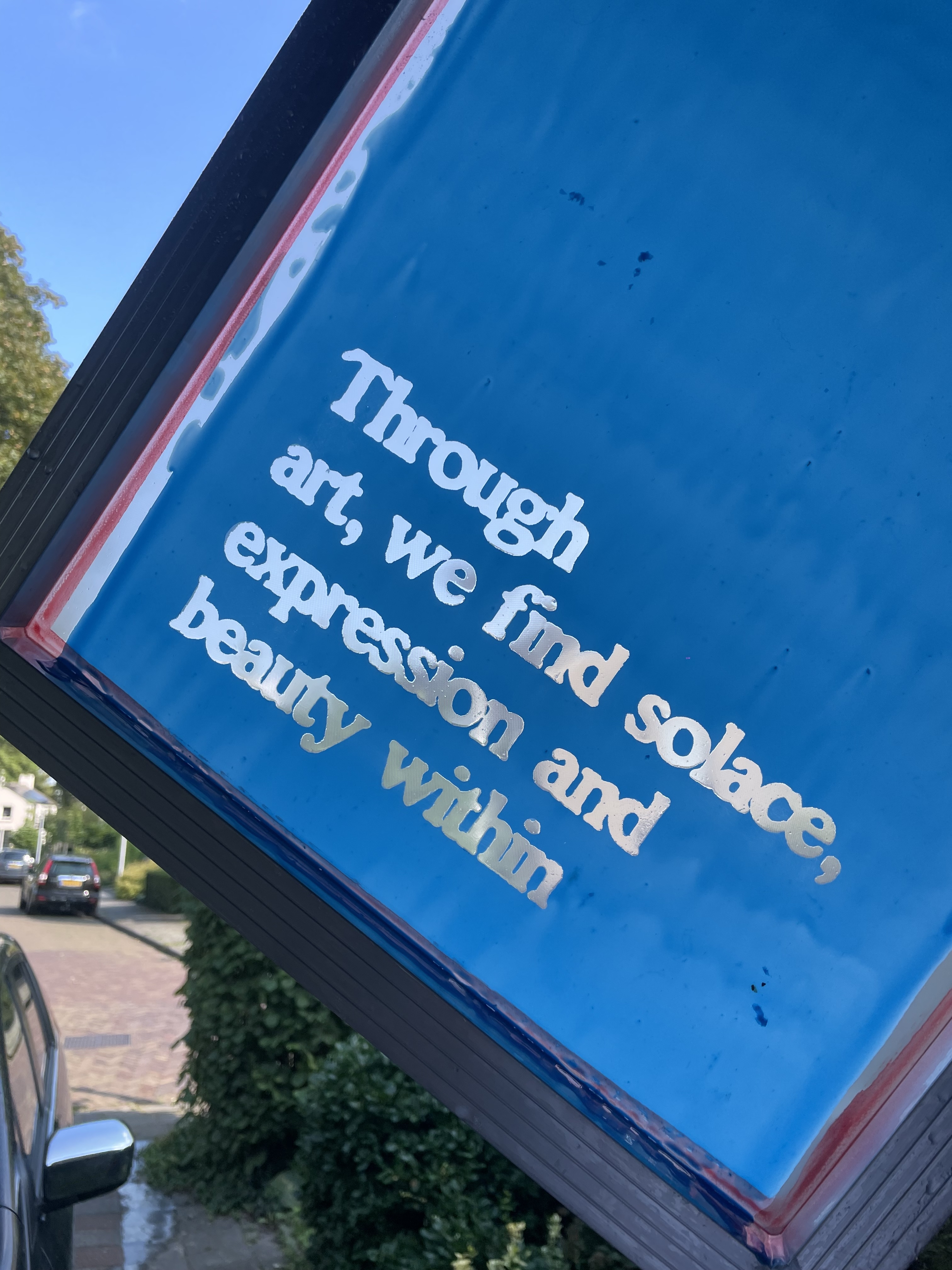 Foto van een zeefdruk met blauwe emulsie, in de zeef is de text: Trough art, we find solace, expression and beatu within. 